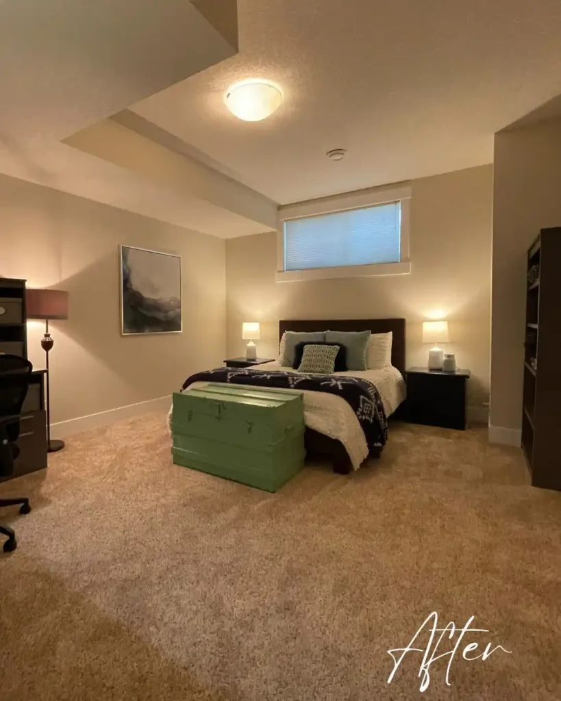 Basement guest bedroom with soft lighting, neutral walls, and vintage storage trunk.