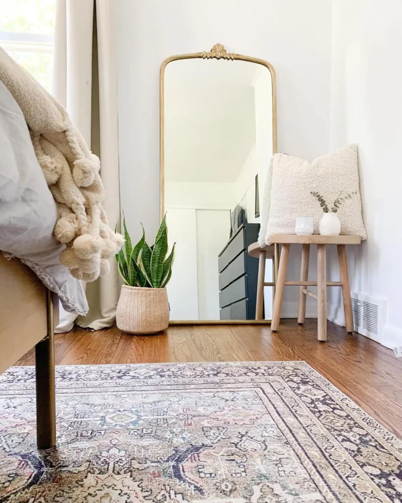 Full length mirror in bedroom with cozy throw, plant, and wooden stool