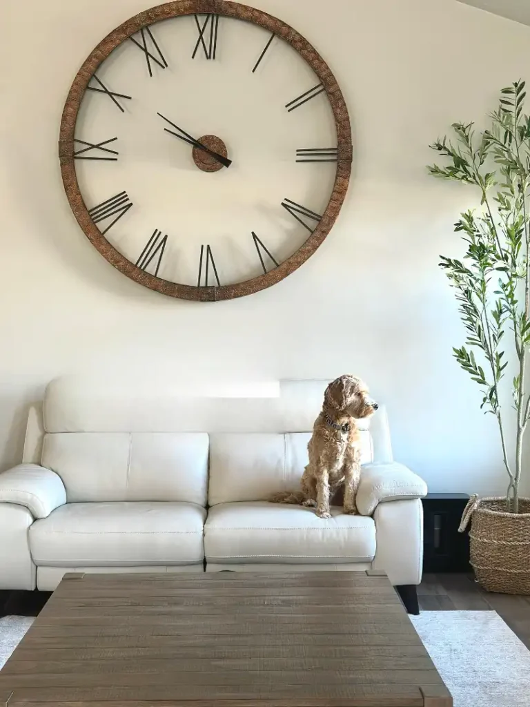 Large rustic wall clock above white sofa in living room for timeless wall decor ideas above couch.
