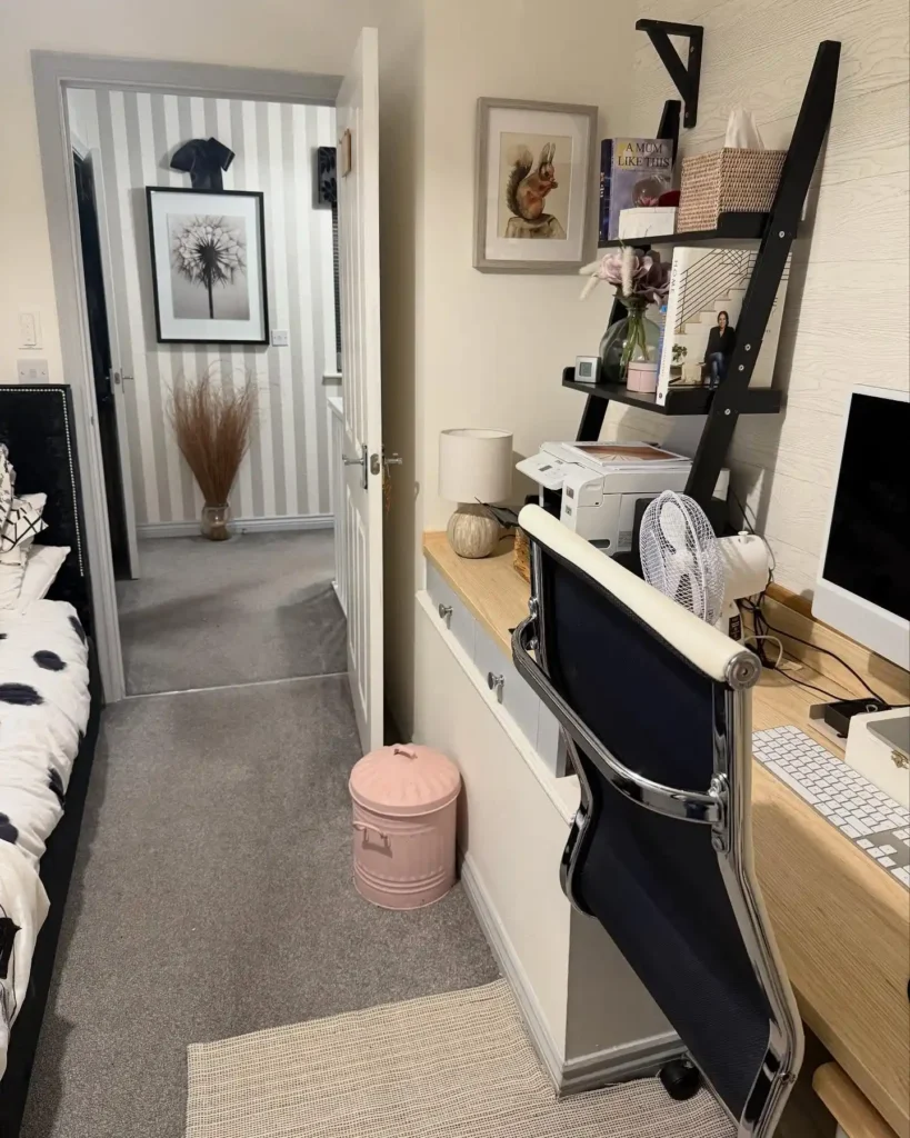 Guest bedroom office combo with black tufted bed, wooden desk, and ladder-style shelving in a cozy, multifunctional layout.