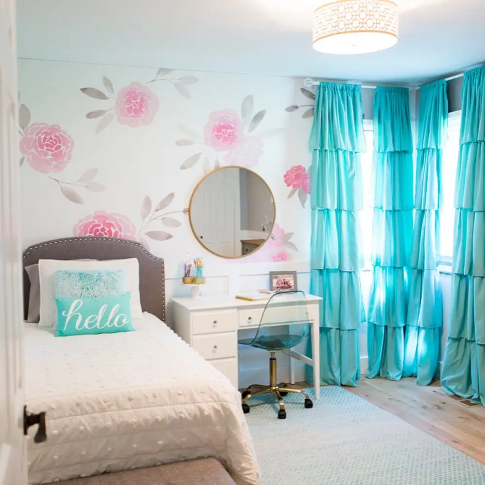 Preteen girls bedroom featuring aqua ruffled curtains, floral wall mural, white bedding, and a cozy desk setup.
