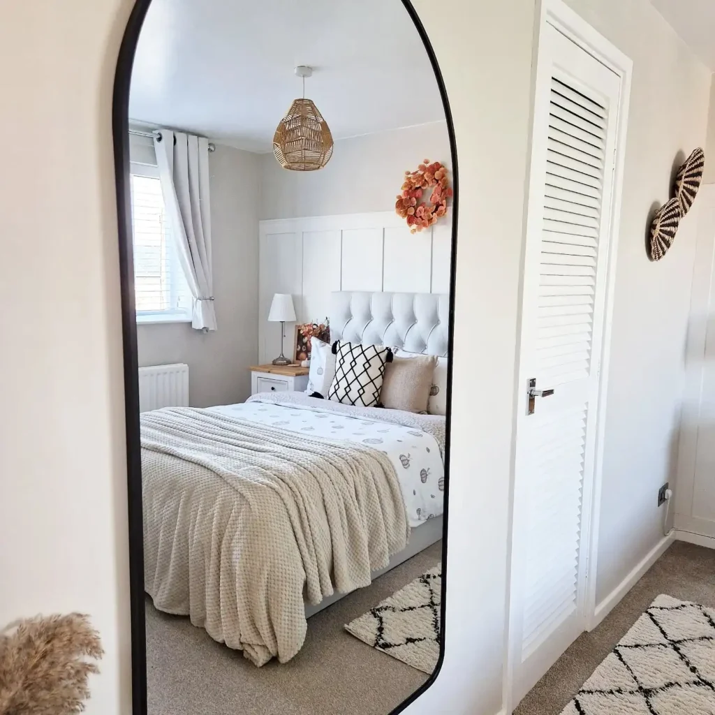 Modern full length mirror in bedroom with black arched frame and cozy neutral decor