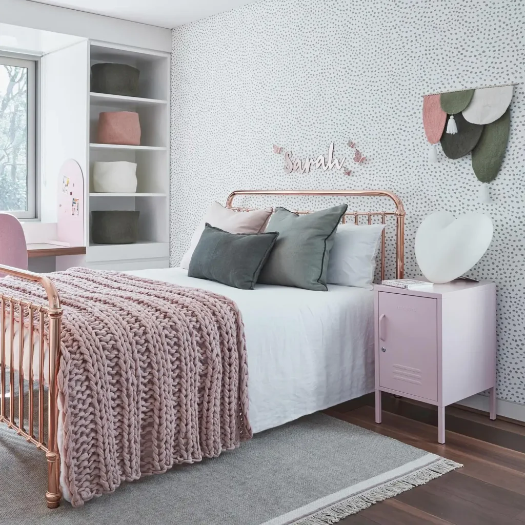 Preteen girls bedroom with rose gold bed frame, blush chunky knit blanket, dotted wallpaper, and personalized name wall art.
