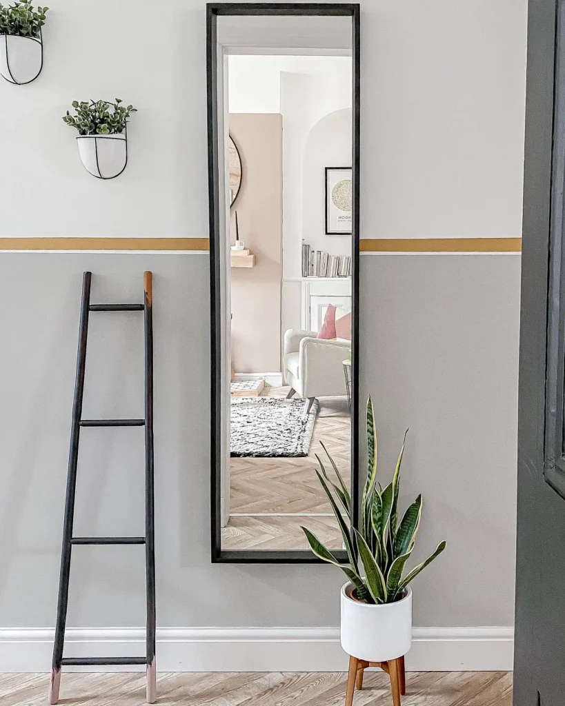 Narrow full length mirror in bedroom with black frame, ladder décor, and plant.