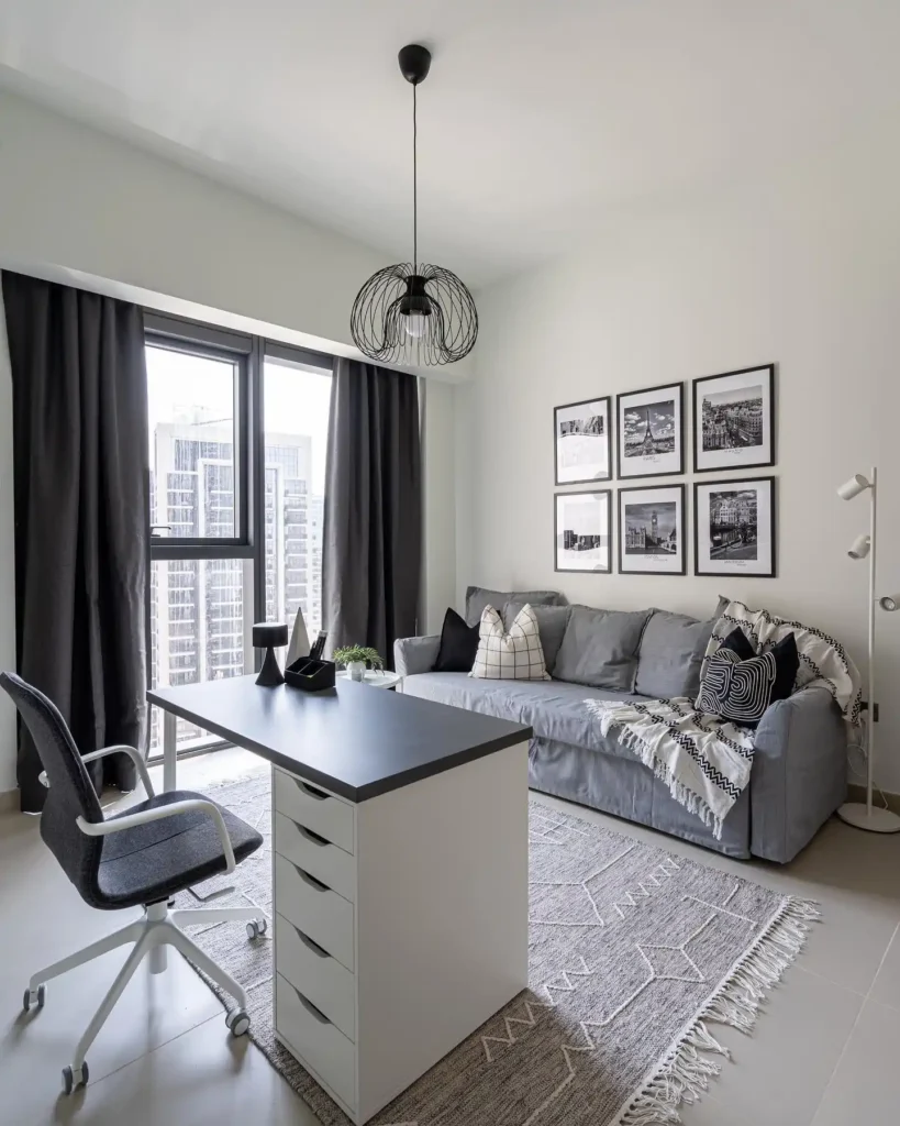 Guest bedroom office combo with sleek gray sofa, wall art, and minimalist desk setup.