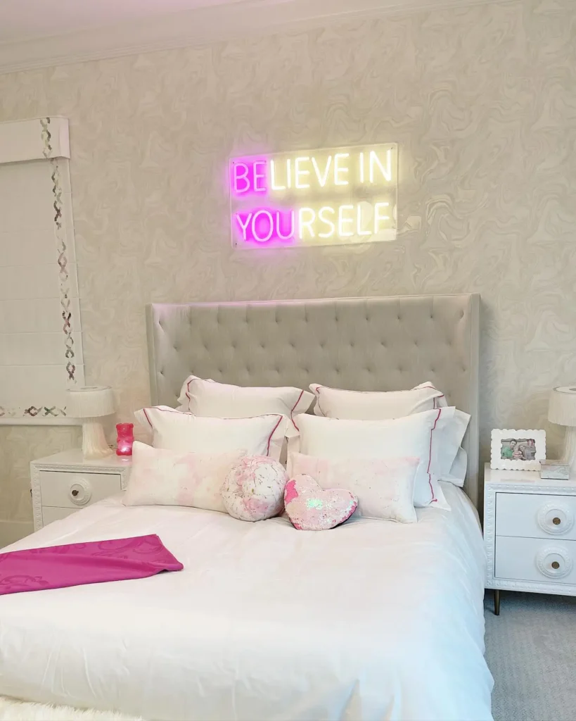 Preteen girls bedroom with tufted headboard, neon wall sign, white bedding, and heart-shaped pillows.
