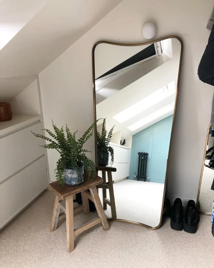 Bedroom with curved-edge full length mirror leaning against wall and rustic stool with plant.