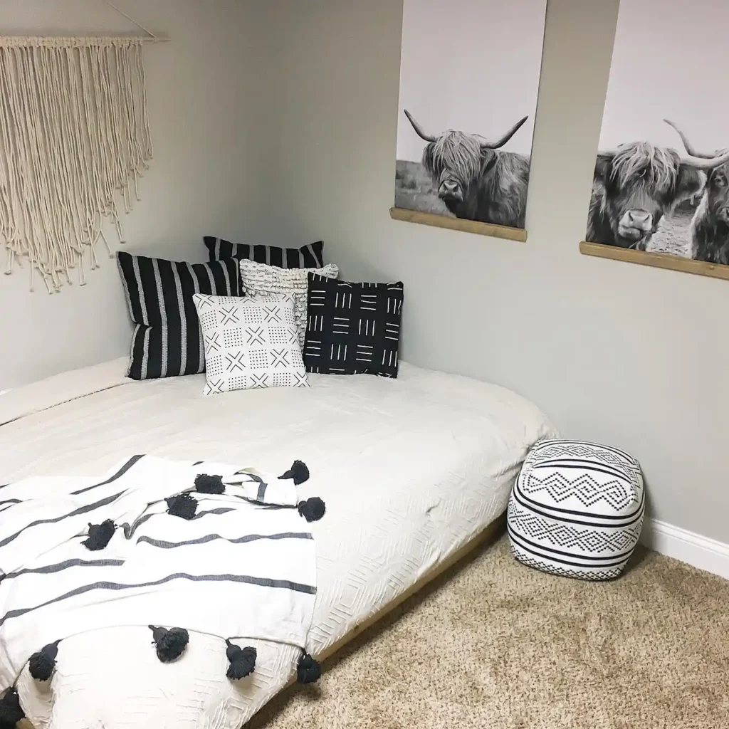Basement guest bedroom with gold lamp, gray headboard, and patterned cushions.