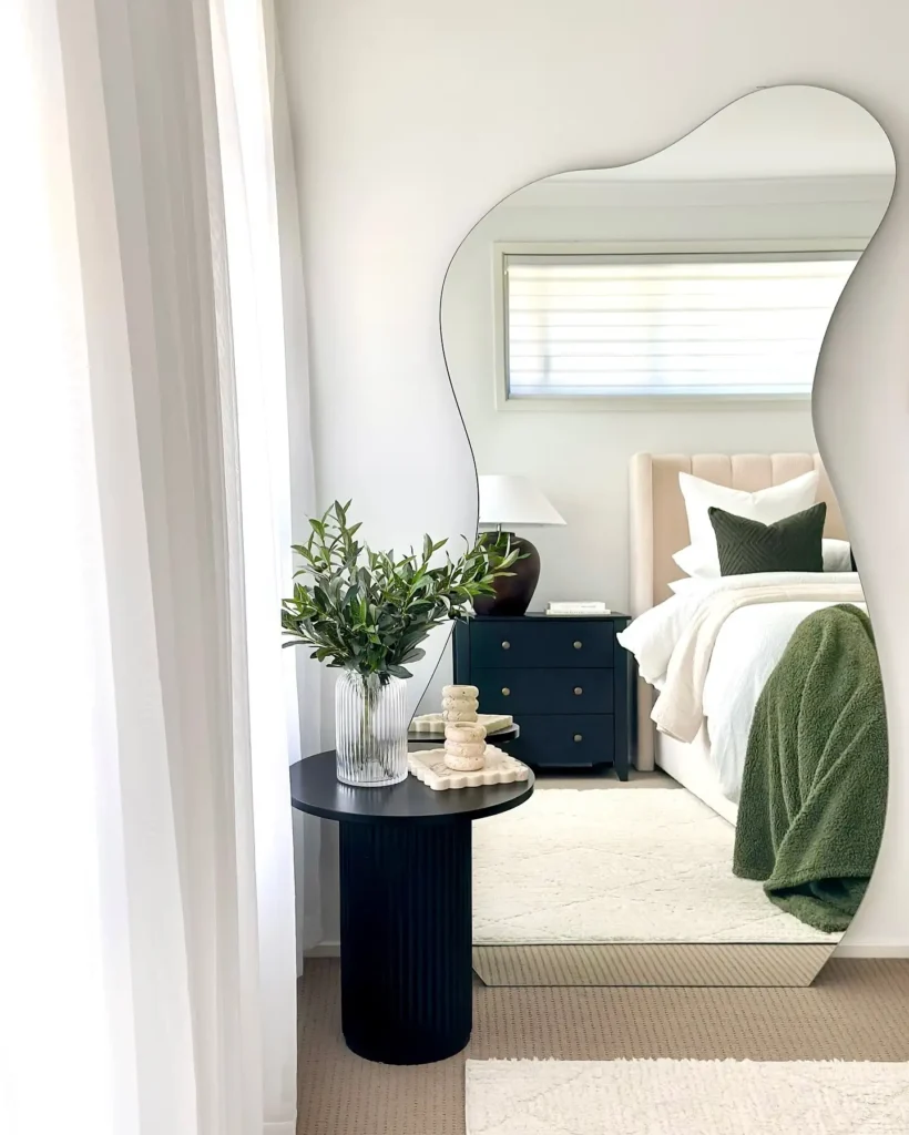 Bedroom with sculptural wavy full length mirror and modern black side table with décor.
