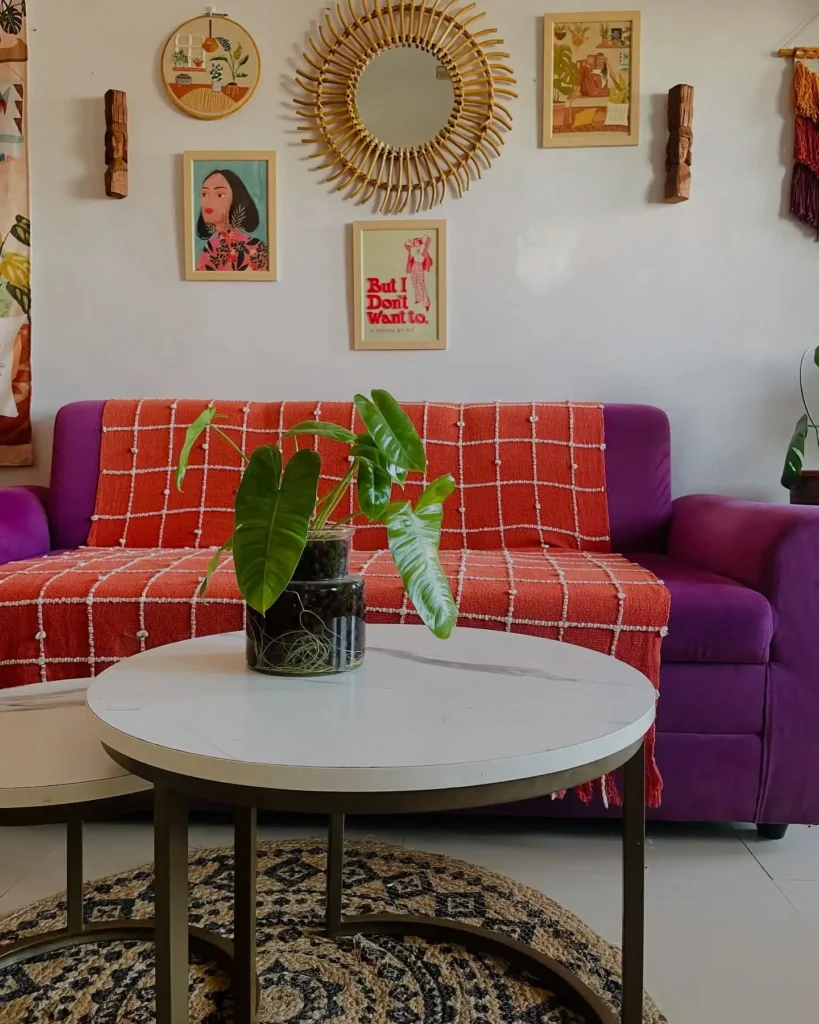 Vibrant living room with purple sofa, orange throw, and eclectic mix of wall art above couch.

