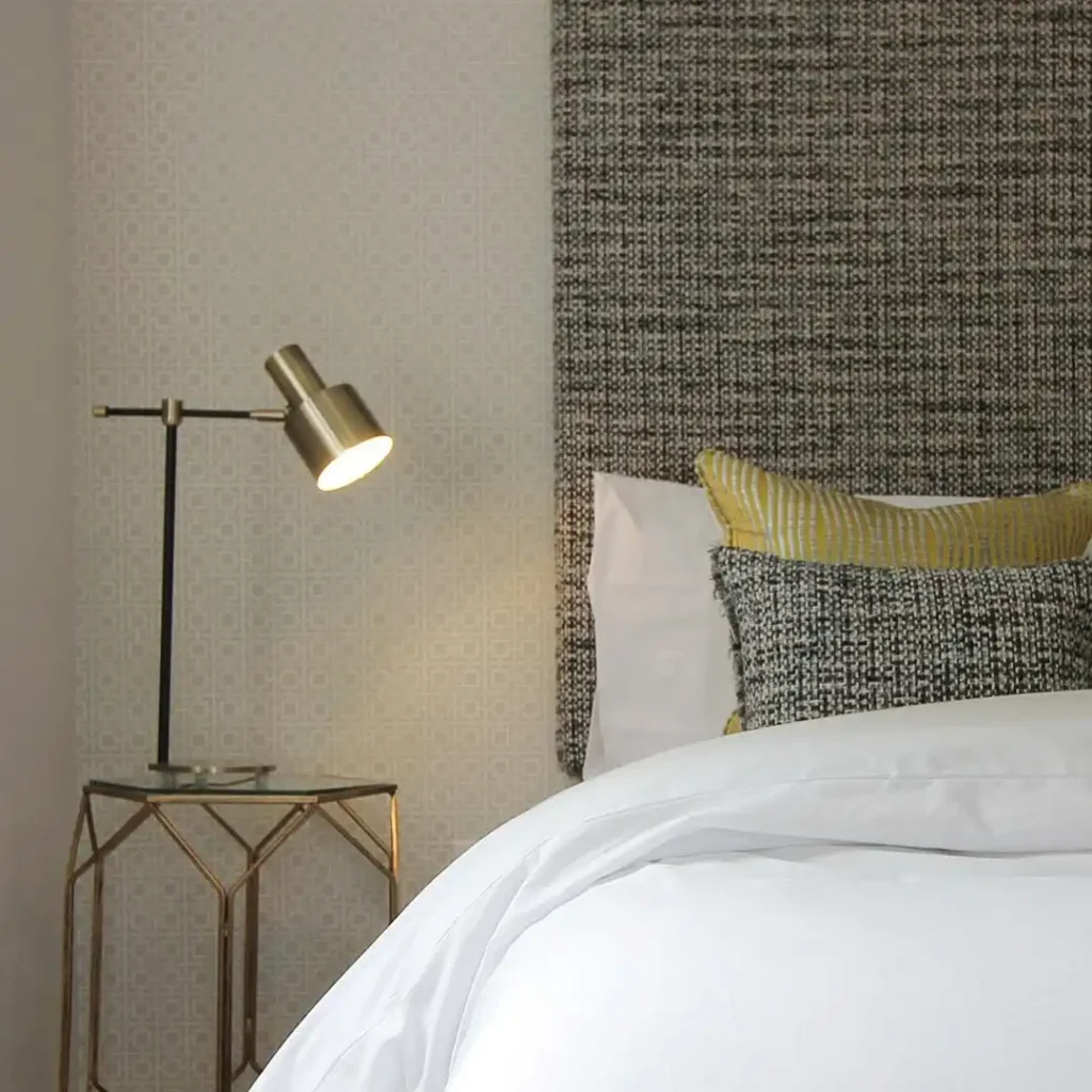 Guest bedroom with modern lamp, metallic side table, and textured pillows.