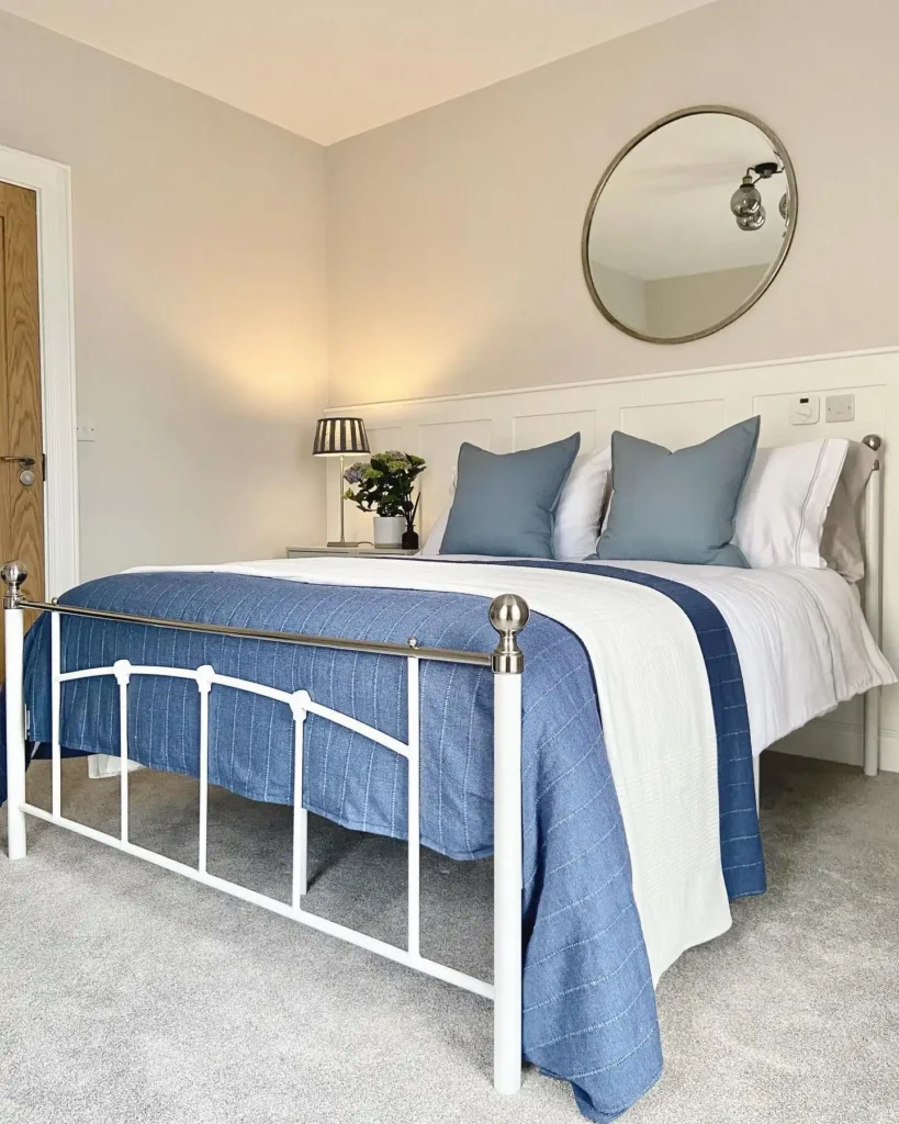 Guest bedroom idea on a budget with white bed frame, blue bedding, and round mirror décor.