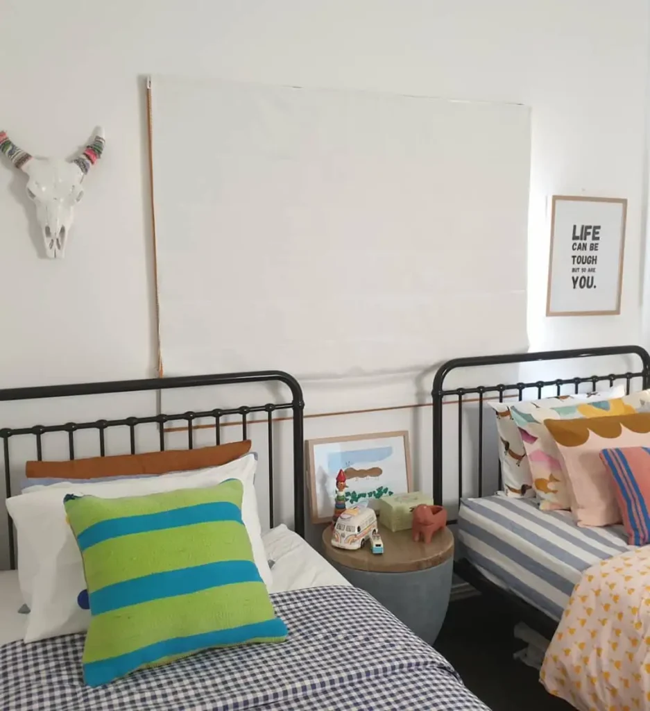 Boy and girl shared bedroom with black metal beds, colorful bedding, and eclectic wall art.
