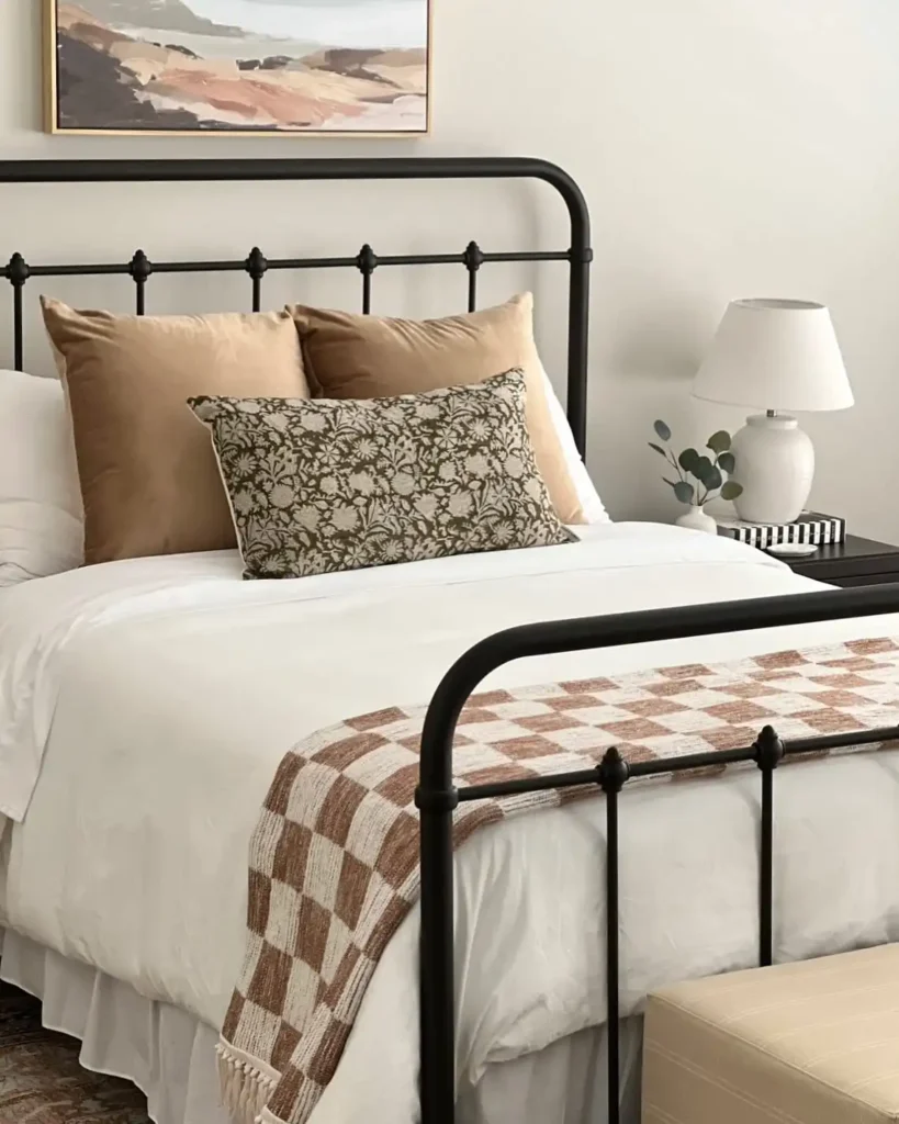 Guest bedroom with black bed frame, beige pillows, and warm wall art.