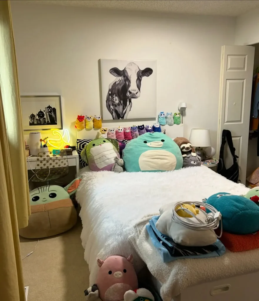 Preteen girls bedroom filled with plush toys, cow wall art, neon lights, and cozy white bedding.
