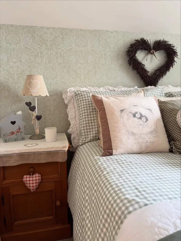 Cottage-inspired guest bedroom idea on a budget with gingham bedding, wooden side table, and rustic heart décor.