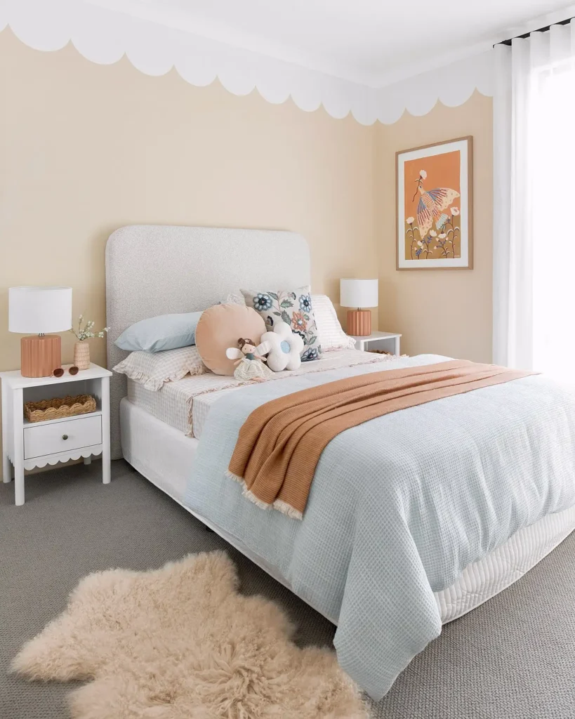 Preteen girls bedroom featuring scalloped wall design, soft pastel bedding, cozy throw blanket, and playful art.
