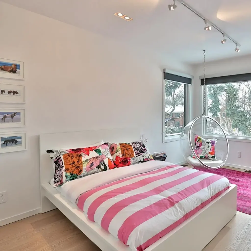 Preteen girls bedroom with striped pink bedding, floral pillows, modern hanging chair, and bright accent rug.