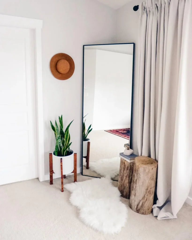 Full length mirror in bedroom with black frame, snake plant, and rustic wood stools