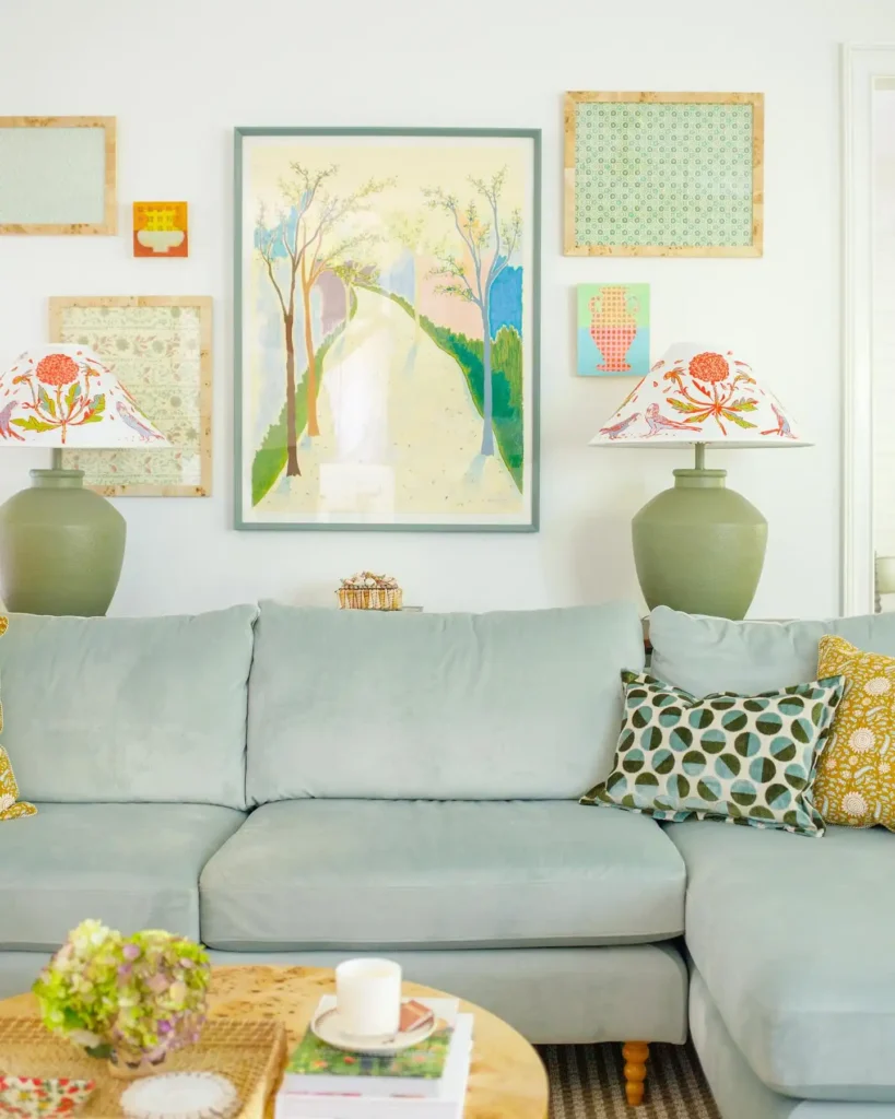 Eclectic gallery wall with framed art and patterned lamps above pastel sofa for cheerful living room wall decor ideas above couch.
