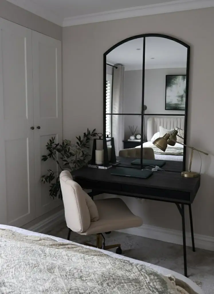 Guest bedroom office combo featuring a black desk, tufted bed, brass lamp, and neutral decor with built-in wardrobe.