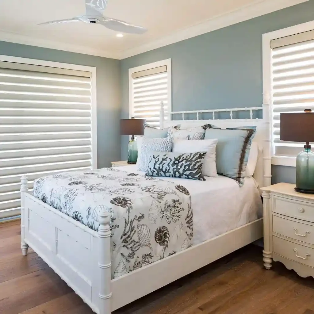 Guest bedroom bedding with seashell-patterned quilt, blue accents, and white wooden bed.
