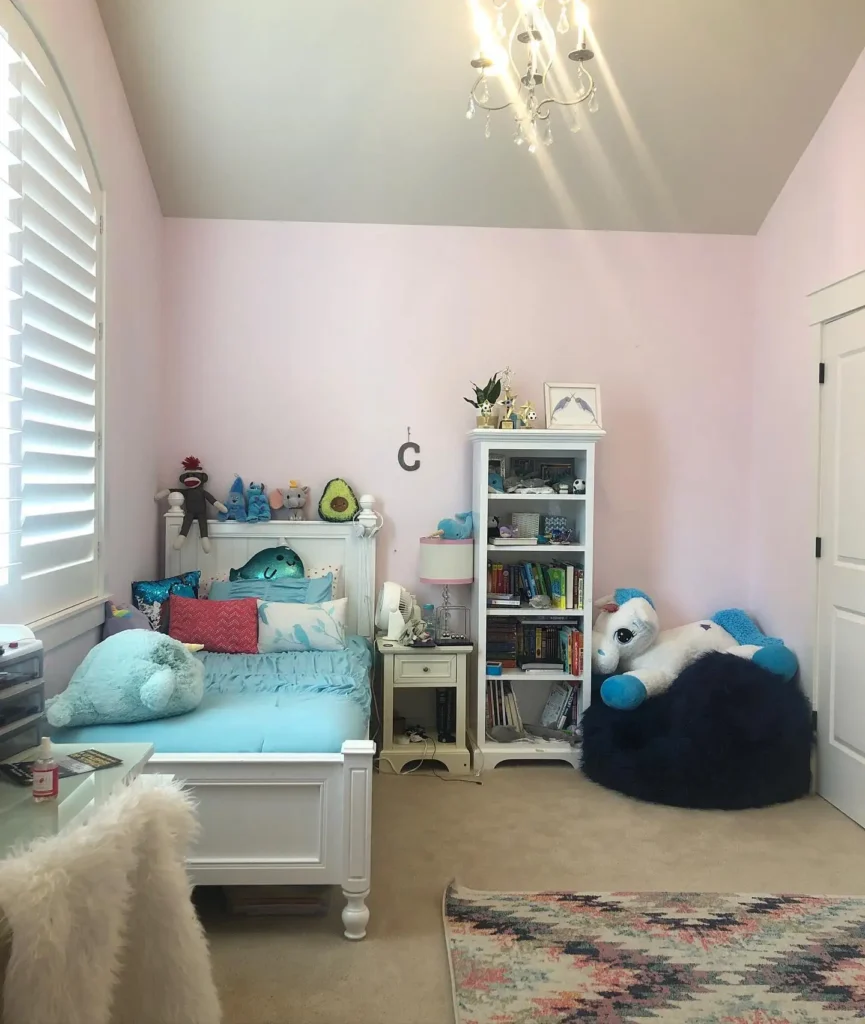 Preteen girls bedroom with aqua bedding, pastel pink walls, plush panda bean bag, and bookshelf for storage.

