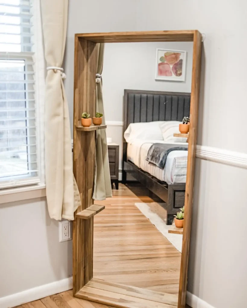 Wooden full length mirror in bedroom with built-in side shelves holding small plants.