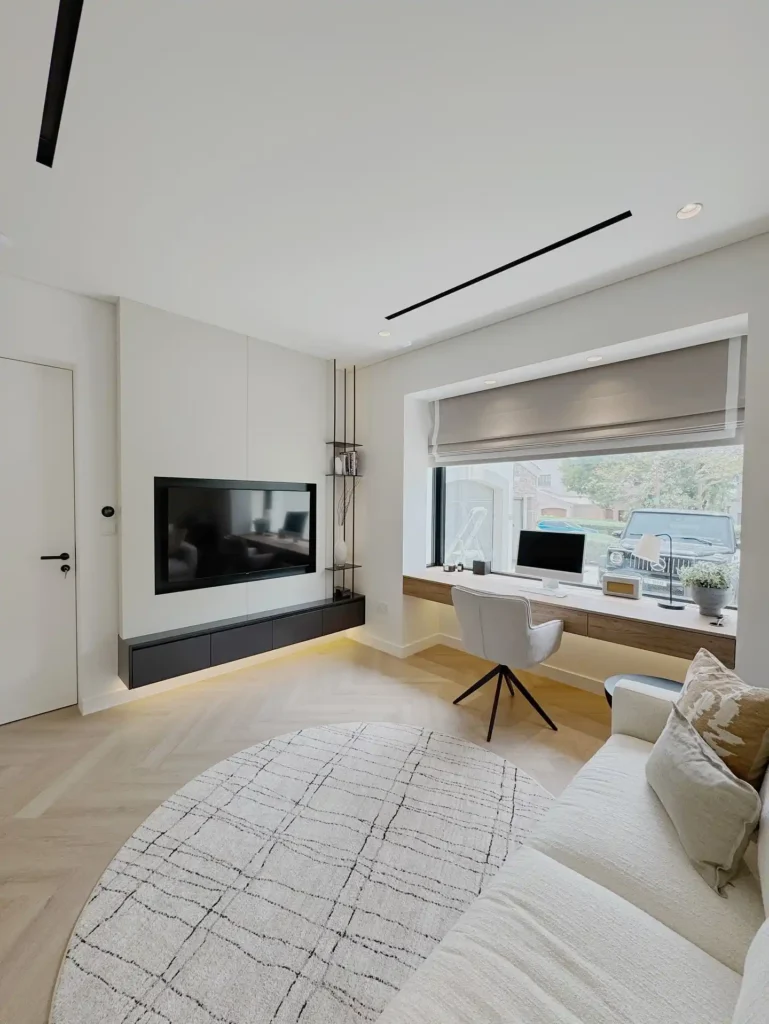 Guest bedroom office combo featuring window desk, neutral sofa, and natural light.