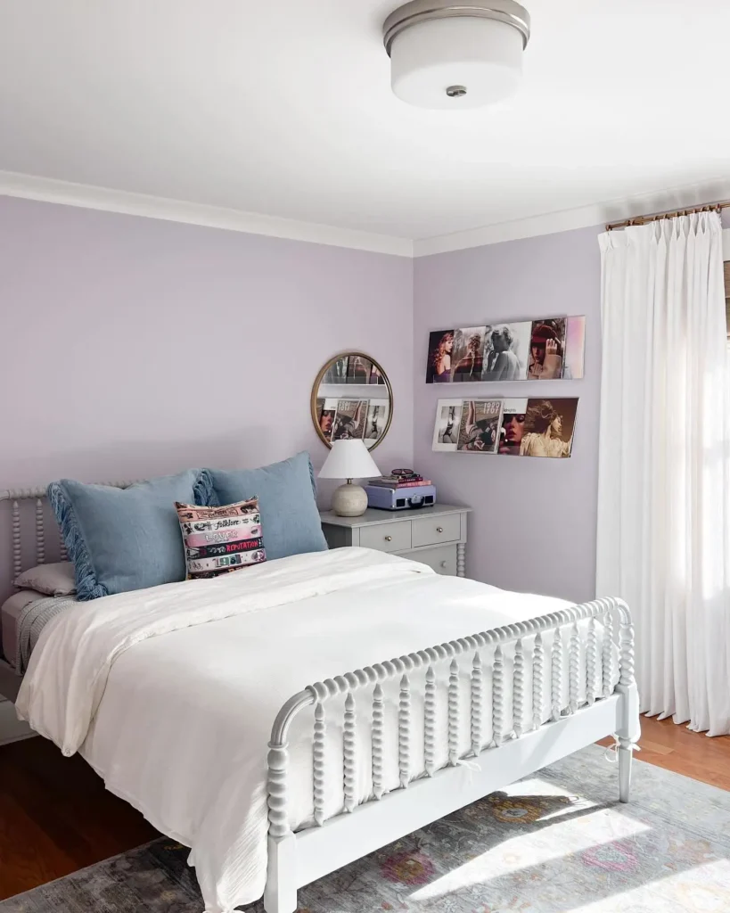 Lavender preteen girls bedroom with spindle bed, white bedding, wall-mounted photo prints, and blue pillows.
