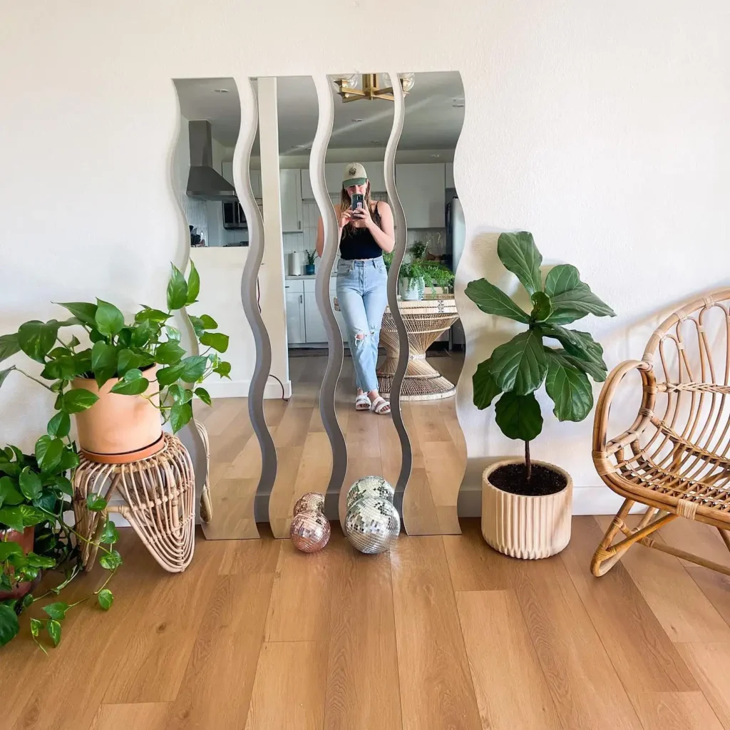 Wavy panel full length mirror with indoor plants and boho rattan furniture in bedroom.