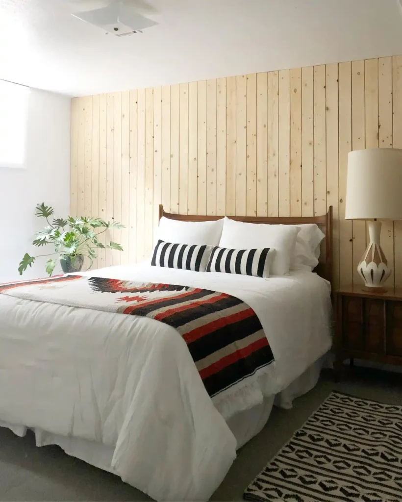 Basement guest bedroom with wood-paneled feature wall and patterned throw.
