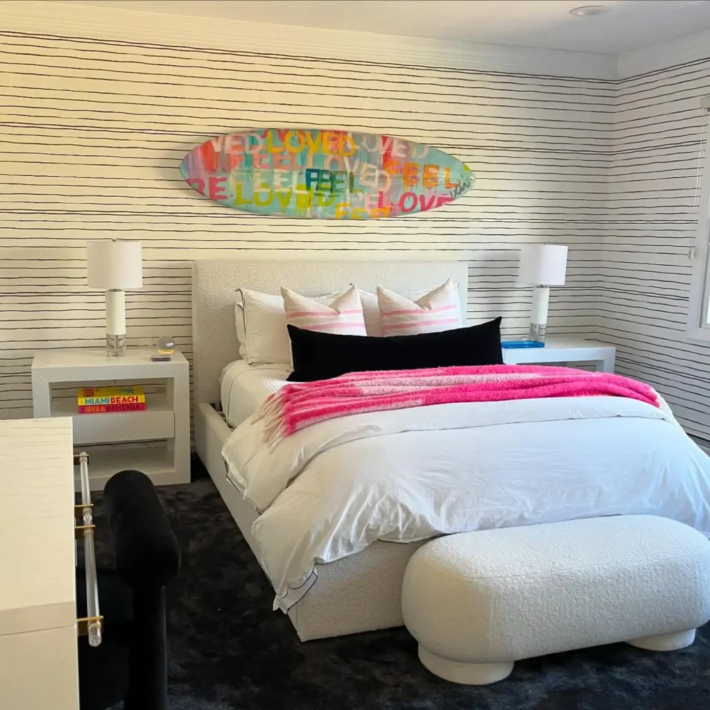 Preteen girls bedroom with striped wallpaper, surfboard-inspired art, white upholstered bed, and pink accents.
