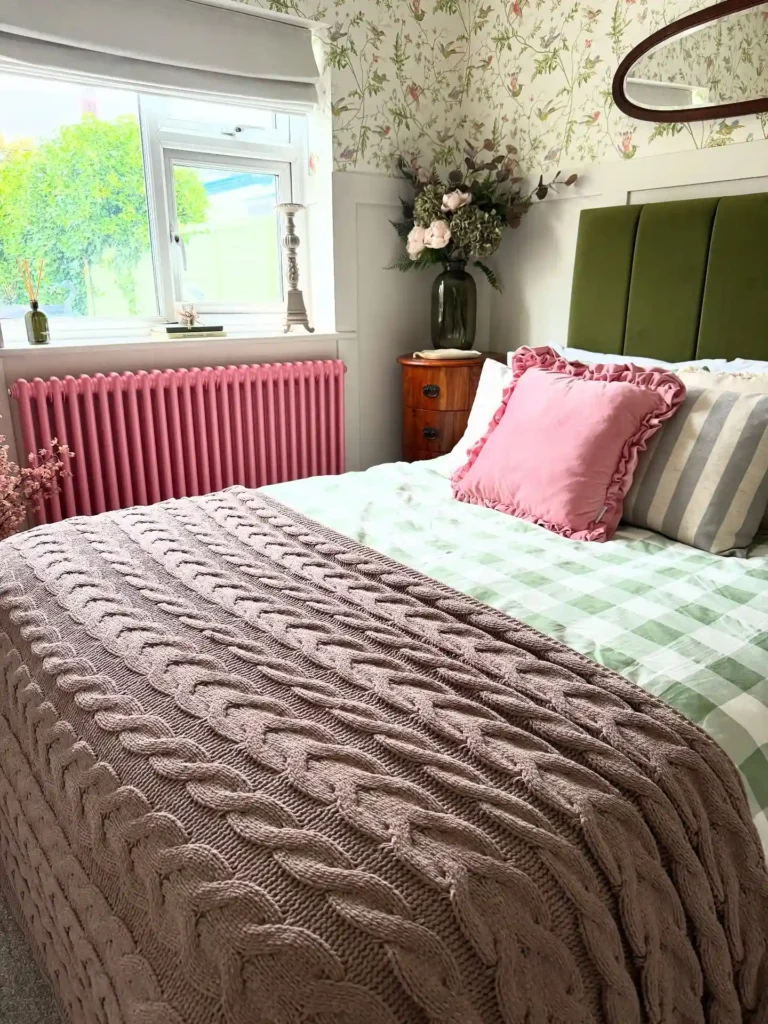 Guest bedroom bedding with plaid sheets, pink pillow, and floral wallpaper.
