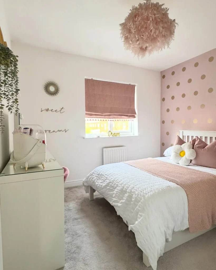 Preteen girls bedroom with pink and gold polka dot wall, white bedding, blush pillows, and fluffy pendant light.
