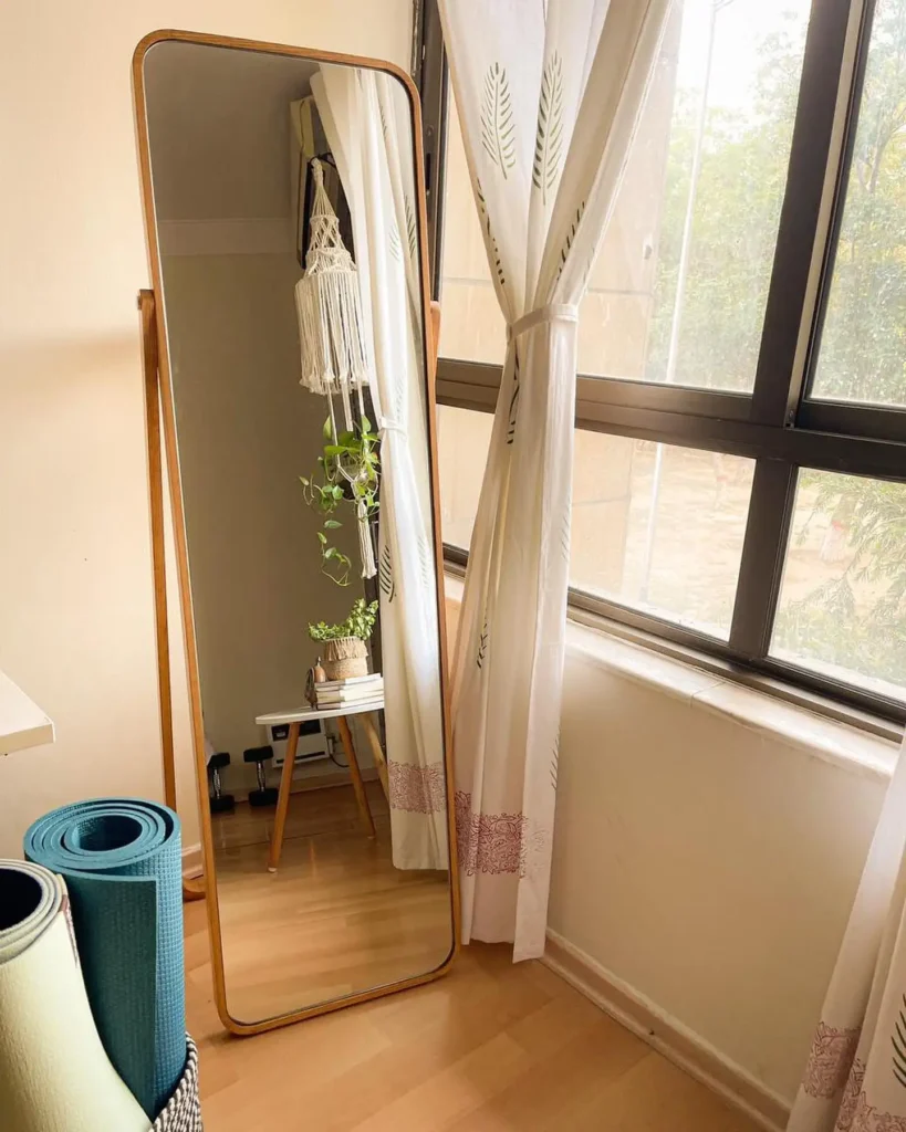 Simple wooden framed full length mirror near large windows with natural light.