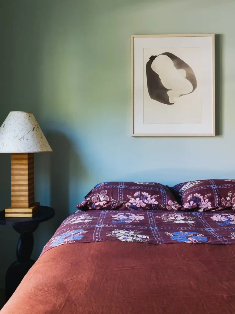 Guest bedroom bedding in burgundy tones with floral print and modern wall art.