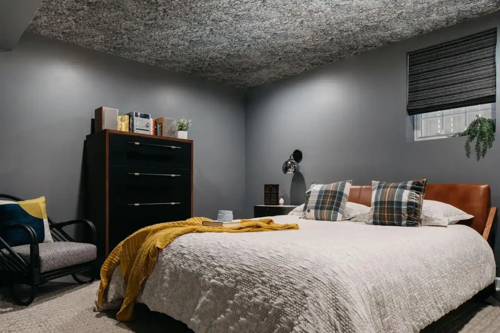 Basement Guest bedroom with dark gray walls, plaid pillows, and warm wooden furniture.