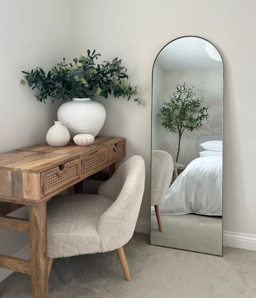 Narrow full length mirror beside wooden desk with greenery and soft neutral tones.