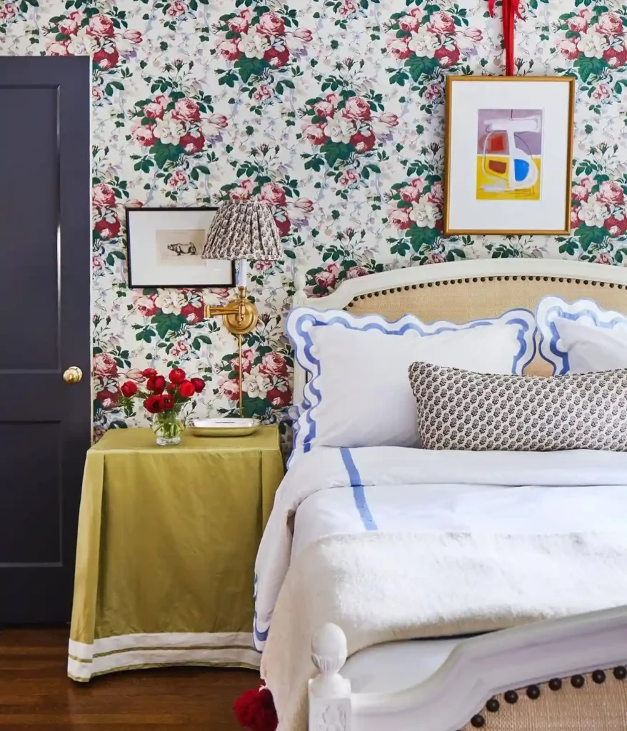 Guest bedroom bedding with crisp white duvet, blue trim pillows, and floral wallpaper.