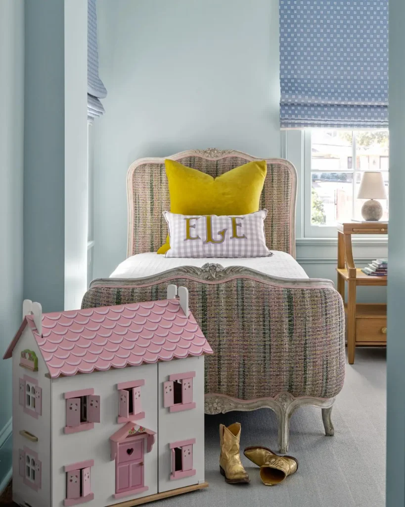 Preteen girls bedroom with plaid bedframe, yellow pillow, vintage dollhouse decor, and soft blue walls.
