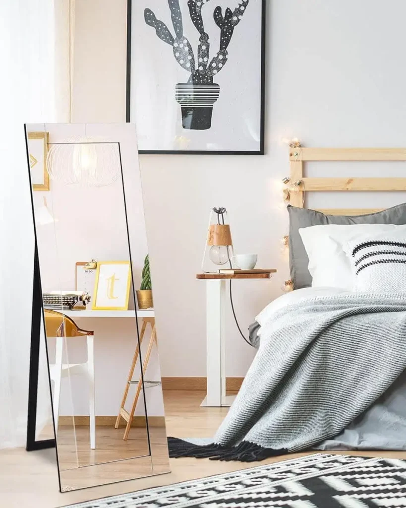Slim framed angled full length mirror leaning against wall beside bed.