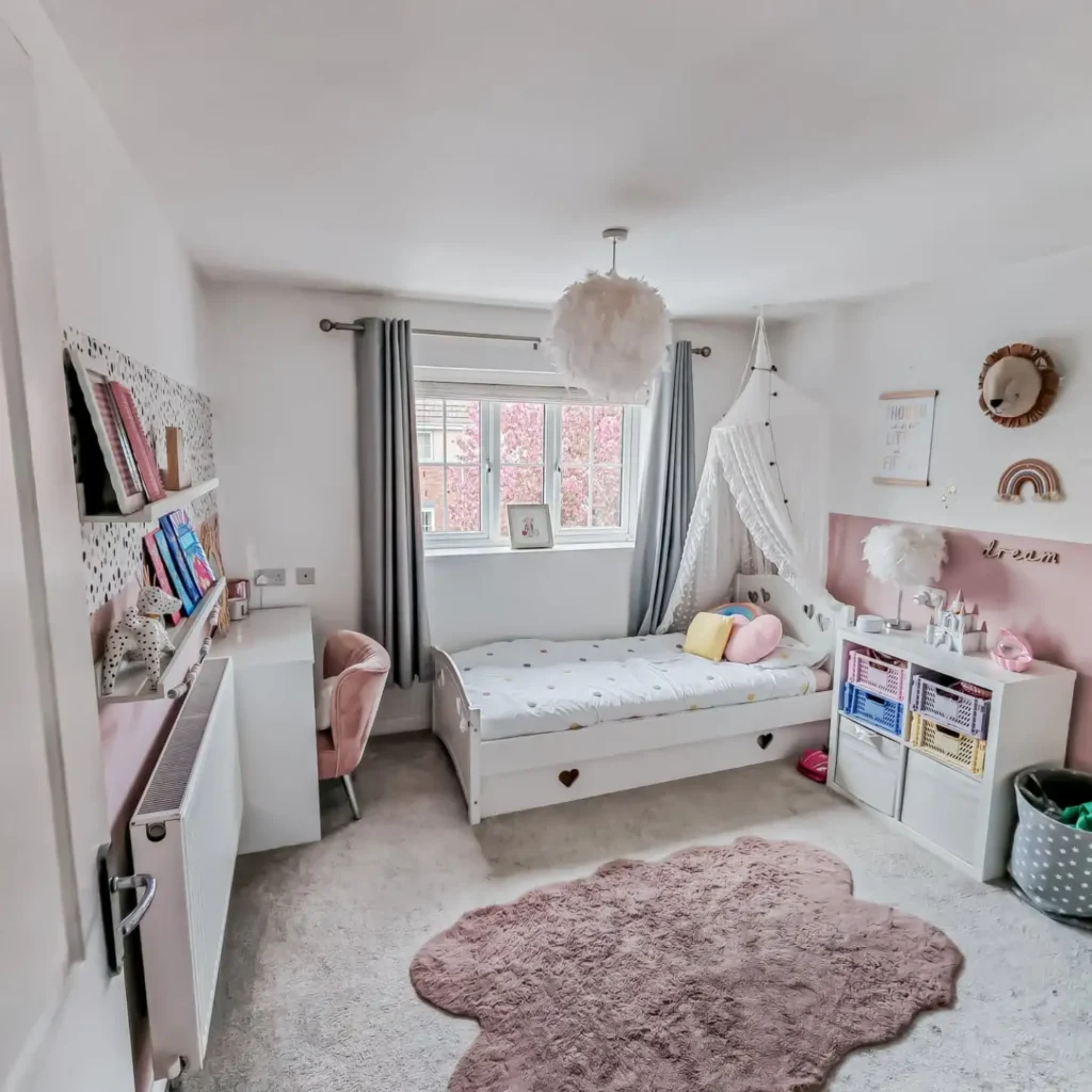 Preteen girls bedroom with canopy bed, pink rug, open shelves, and feather pendant light.
