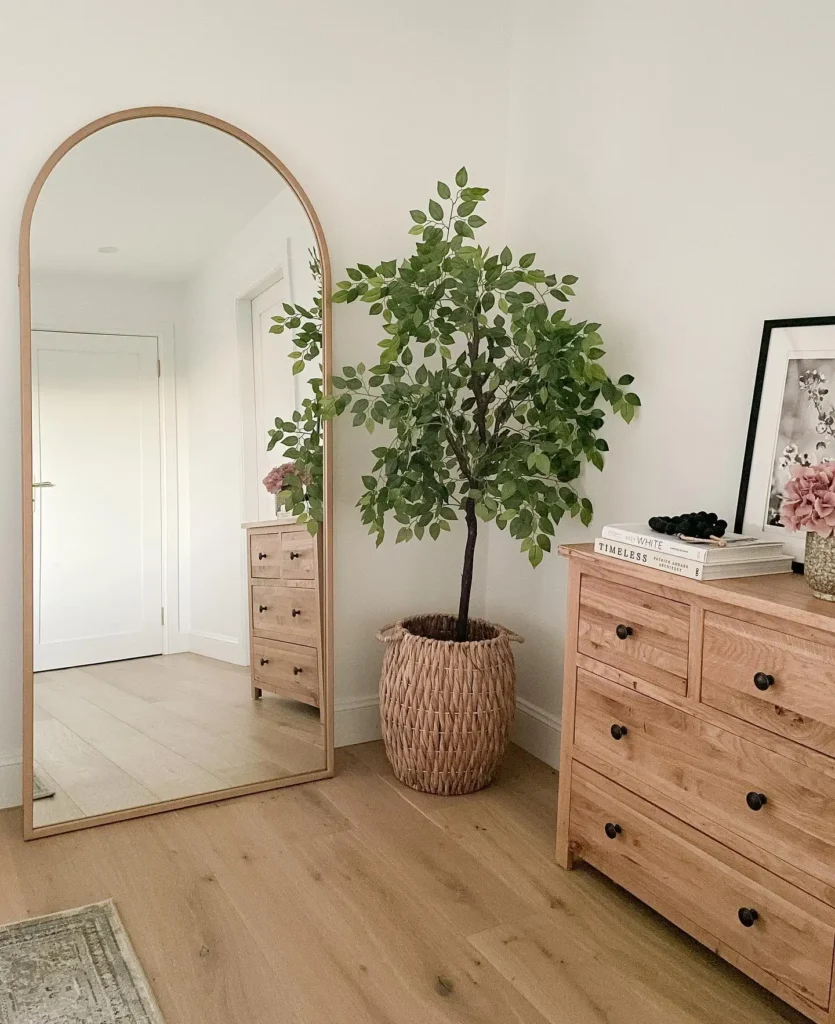 Full length mirror in bedroom with arched wooden frame and natural dresser
