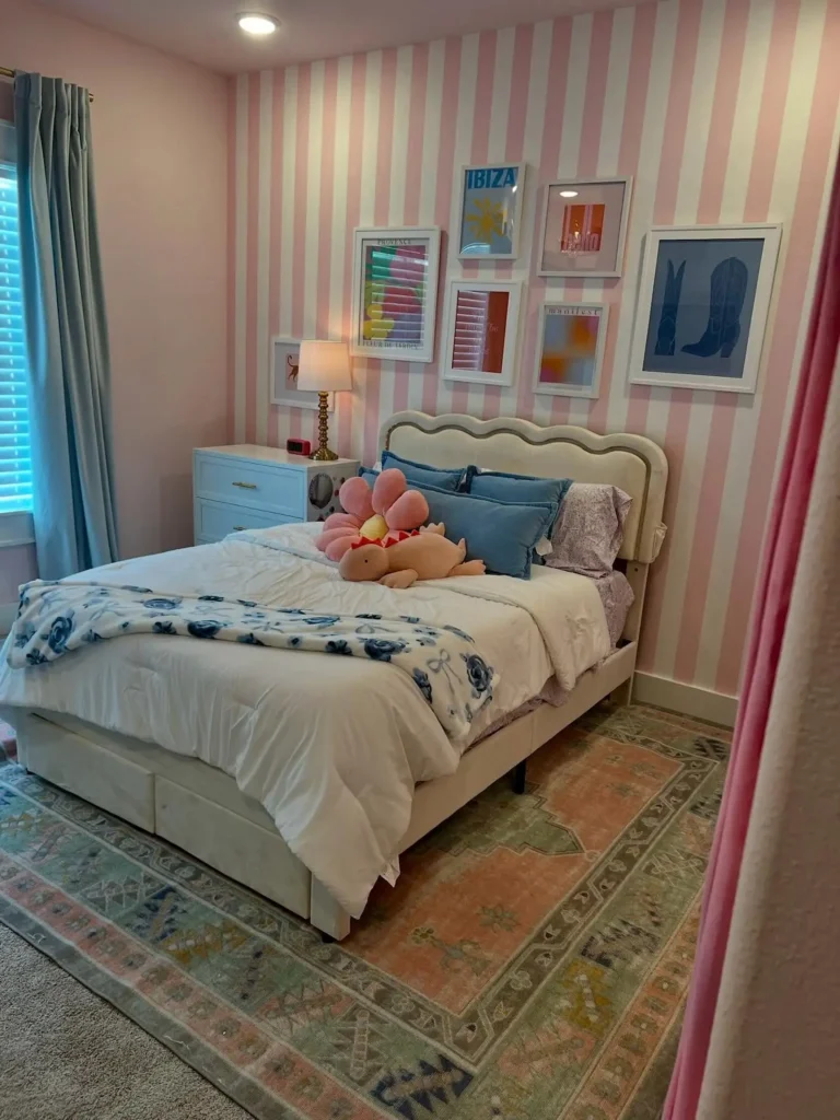 Preteen girls bedroom with striped wallpaper, framed artwork, blue curtains, and pink rug.
