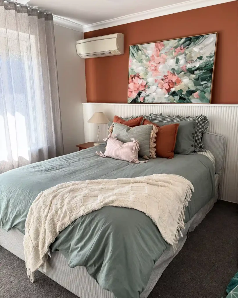 Guest bedroom bedding in sage green with terracotta pillows and abstract wall art.
