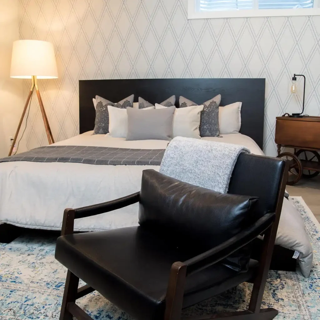 bedroom with diamond-patterned wallpaper, gray bedding, and cozy chair.
