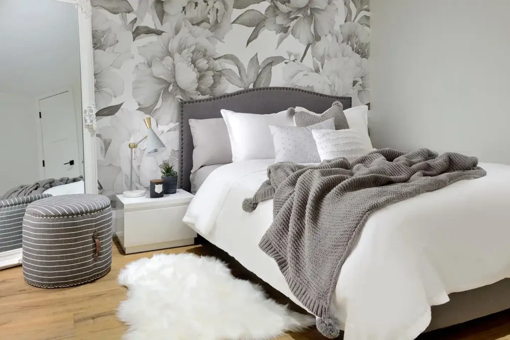 Basement bedroom with floral wallpaper, white bed, and gray blanket.
