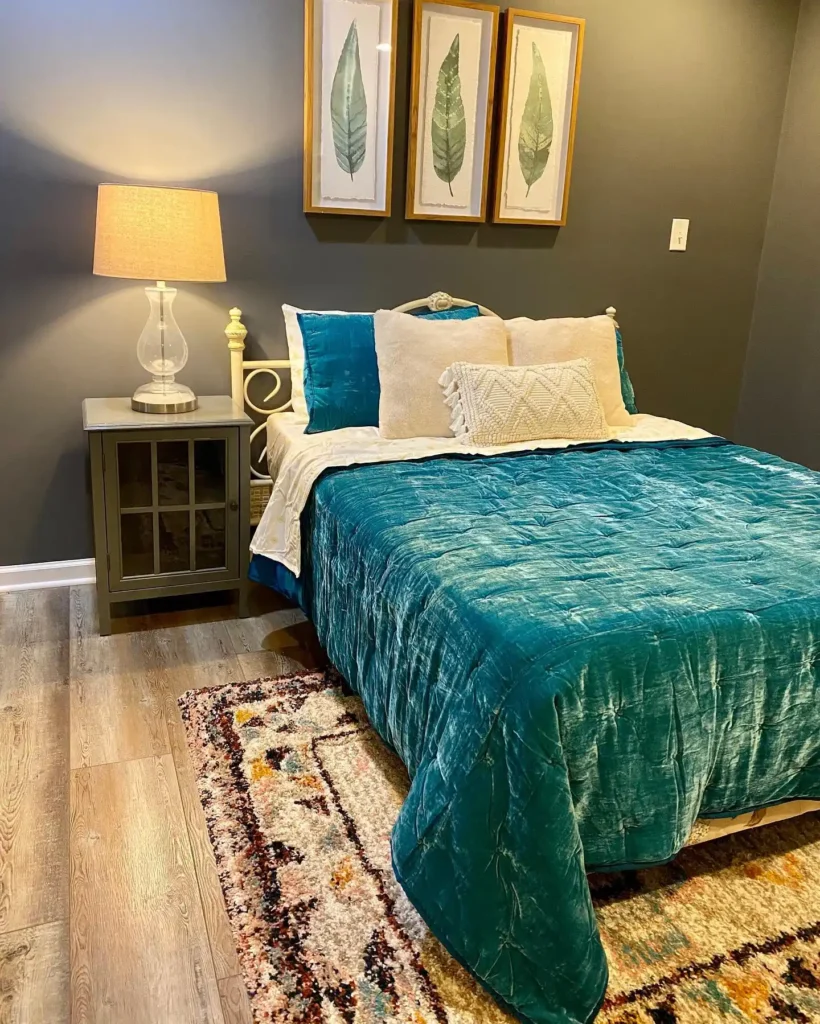 Basement guest bedroom with teal bedding, dark walls, and framed botanical art.
