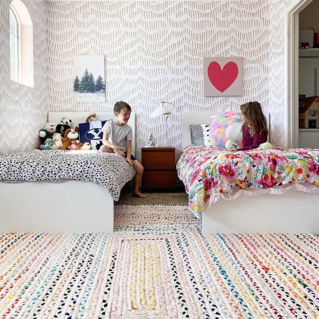 Boy and girl shared bedroom with mismatched bedding, colorful rug, and playful wall art.
